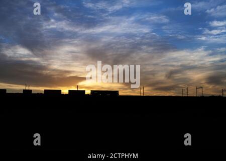 Silhouette di una locomotiva DC Cargo Rail classe 66 Un treno merci intermodale per container sulla linea principale della costa occidentale all'alba Foto Stock