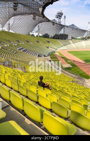 Monaco, Baviera / Germania - 17 settembre 2020: Una donna singola con lunghi capelli castani seduta da sola in uno stadio gigante e vuoto Foto Stock