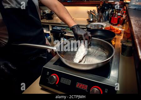 chef sta friggendo il triglia in una padella su una stufa elettrica. Cucina di pesce nel caffè. Foto Stock