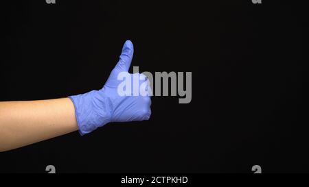 La mano femminile in un guanto medico di lattice fa un simile movimento isolato su sfondo nero Foto Stock