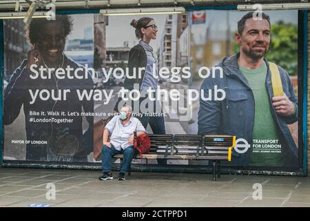 PUTNEY LONDON, REGNO UNITO. 23 Settembre 2020. Un uomo seduto di fronte a un grande poster pubblicizzato dal sindaco di Londra in una stazione della metropolitana recita 'Stretch le gambe sulla strada per il pub. Il governo ha inasprito le restrizioni in quanto i pub sono ordinati per chiudere entro le 22 per fermare la diffusione del covid-19 a seguito dell'aumento delle infezioni da coronavirus Credit: amer Ghazzal/Alamy Live News Foto Stock