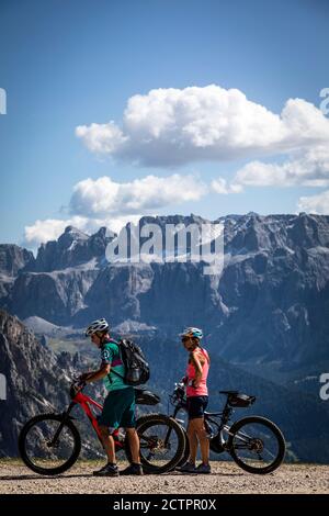 Due ciclisti con mountain bike ammirano la vista del Massiccio del Sella fuori dalla stazione della funivia Seceda , Val Gardena, Italia. Foto Stock