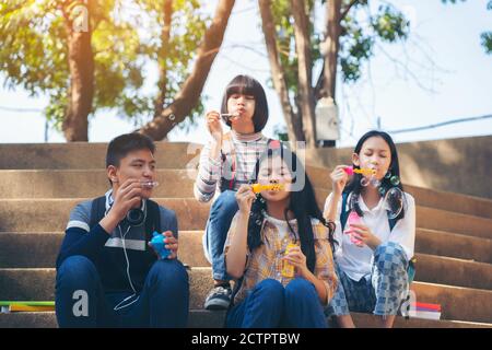 Gruppo di bambini che soffiano bolle di sapone e si divertono dentro parco estivo all'aperto Foto Stock