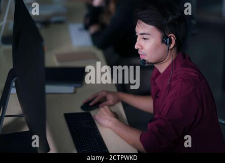 Thai Asian MAN Customer Services operatori di assistenza lavorano turno notturno nel call center per aiutare il cliente di assistenza sul posto di lavoro di notte, amichevole Foto Stock