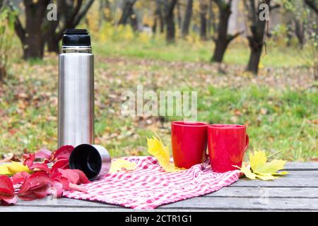 Picnic d'autunno, coppa rossa con thermos su un tavolo di legno. Concetto d'autunno romantico Foto Stock