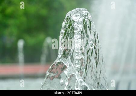 Immagine in primo piano di una fontana d'acqua in un parco cittadino su uno sfondo di alberi verdi Foto Stock