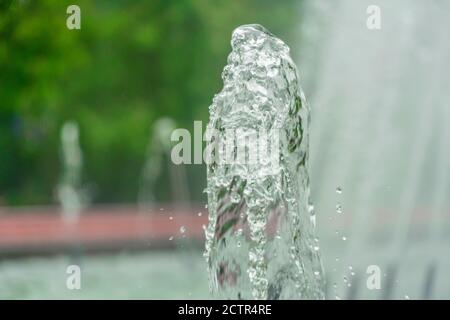 Immagine in primo piano di una fontana d'acqua in un parco cittadino su uno sfondo di alberi verdi Foto Stock