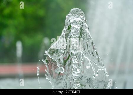 Immagine in primo piano di una fontana d'acqua in un parco cittadino su uno sfondo di alberi verdi Foto Stock