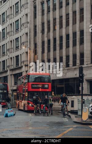 Londra, UK - 24 agosto 2020: Ciclisti e autobus rosso in attesa al semaforo nella City of London, uno storico quartiere finanziario, da Tower Bridge Foto Stock