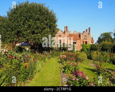 Chenies Manor House Sunken Garden in un pomeriggio soleggiato settembre, 2020. Dahlias colorati, bordi di piante erbacee, prato, trellis di edera; cielo blu. Foto Stock