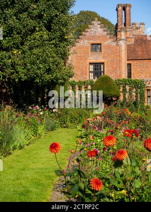 Chenies Manor House Sunken Garden in un pomeriggio soleggiato settembre, 2020. Dahlias colorati, bordi di piante erbacee, prato, trellis di edera; cielo blu. Foto Stock