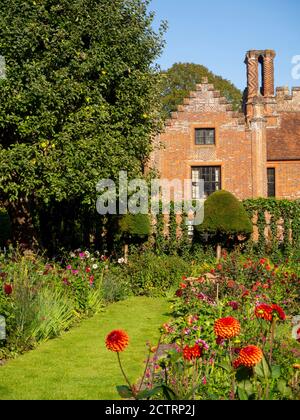 Chenies Manor House Sunken Garden in un pomeriggio soleggiato settembre, 2020. Dahlias colorati, bordi di piante erbacee, prato, trellis di edera; cielo blu. Foto Stock