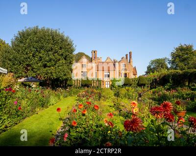 Chenies Manor House Sunken Garden in un pomeriggio soleggiato settembre, 2020. Dahlias colorati, bordi di piante erbacee, prato, trellis di edera; cielo blu. Foto Stock