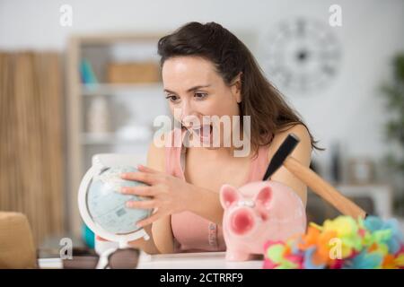 donna che tiene un globo e ha martello messo in testa su piggybank Foto Stock