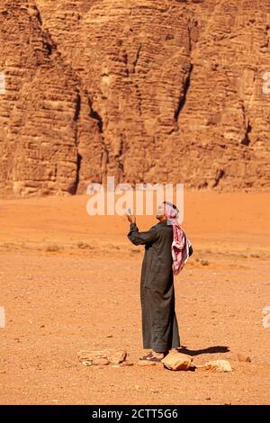 Wadi Rum, Jordan 04/01/2010: Un uomo arabo che indossa tradizionali kefiyeh, agal, occhiali da sole e il tobo di Juba (vestito lungo) sta sollevando il suo telefono cellulare Foto Stock