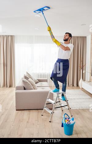 Uomo pulizia soffitto e lampade in soggiorno. Concetto di servizio di pulizia della casa. Foto Stock
