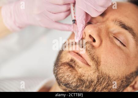 Giovane uomo non rasato che riceve iniezione cosmetica presso il centro benessere Foto Stock