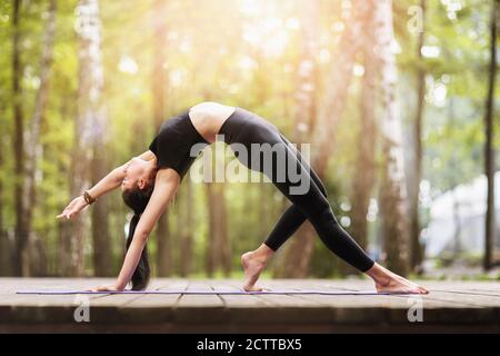 Giovane donna in nero sportivo esegue l'esercizio in ponte nel parco, Camatkarasana asana, danza cane yoga posa Foto Stock