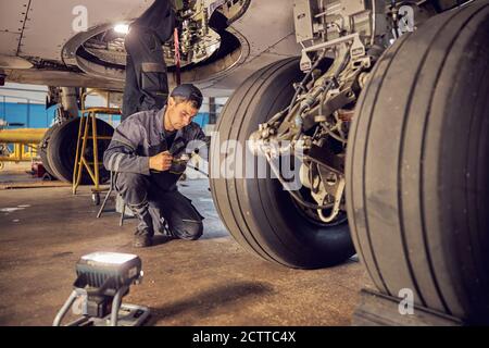 Carrello di atterraggio aereo in gomma telaio hangar con il lavoratore di aviazione in uniforme Foto Stock