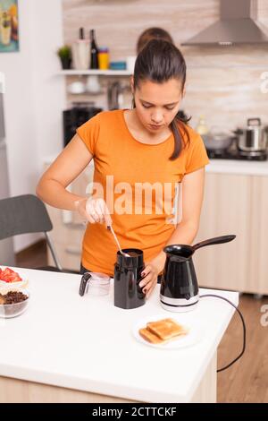 Donna che usa caffè fresco macinato per preparare un caffè deicioso. Uno stile di vita sano, che prepara un pasto delizioso al mattino in una cucina accogliente. Pranzo tradizionale gustoso Foto Stock