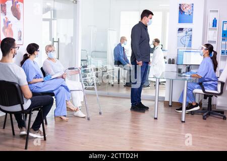 Uomo che discute con l'infermiere alla reception dell'ospedale indossando la maschera facciale come precauzione di sicurezza contro il coronavirus durante la pandemia globale. Uomo, preoccupato, protezione, corona, medicina, Foto Stock