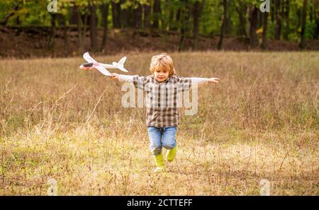 Bambino felice che gioca all'aperto. Happy boy giocare aereo. Ragazzino con aereo. Piccolo capretto sogna di essere un pilota. Bambino che gioca con l'aereo giocattolo Foto Stock