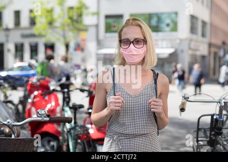 Ritratto di giovane donna casual che cammina per strada indossando maschera protettiva come protezione contro il virus covid-19. Persone incidentali sullo sfondo Foto Stock