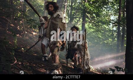 Tribù di cacciatori-raccoglitori indossando animale Skin Holding Stone Tipped Tools, esplorare Preistic Forest in a Hunt for Animal Prey. Famiglia Neanderthal Foto Stock