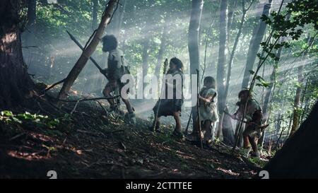 Tribù di cacciatori-raccoglitori indossando animale Skin Holding Stone Tipped Tools, esplorare Preistic Forest in a Hunt for Animal Prey. Famiglia Neanderthal Foto Stock