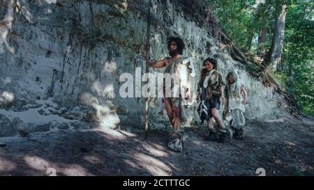 Tribù di cacciatori-raccoglitori che indossano pelle animale che vive in una grotta. Preparare cibo, costruire fuoco, gestire pelli, lavorare, Caccia. Felice Neanderthal Foto Stock