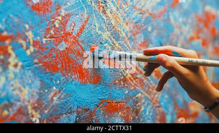 Primo piano di mano di artista femminile, tenendo pennello e disegno pittura con vernice rossa. Pittura ad olio colorata ed emozionale. Pittore contemporaneo Foto Stock