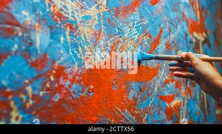 Primo piano di mano di artista femminile, tenendo pennello e disegno pittura con vernice rossa. Pittura ad olio colorata ed emozionale. Pittore contemporaneo Foto Stock