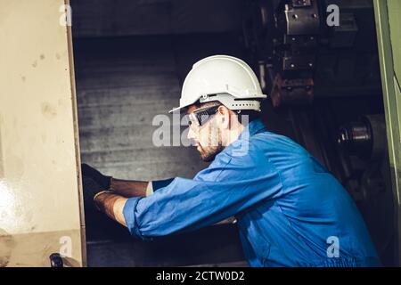 Controllo riparazione e riparazione dei lavoratori tecnici all'interno di una macchina CNC in una fabbrica dell'industria dei metalli pesanti. Foto Stock