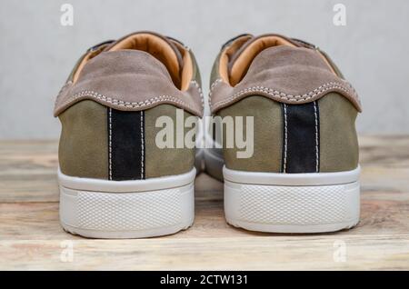 Nuove sneaker da uomo grigio-verde con suole bianche e lacci bianchi su sfondo in legno da vicino. Parte in tacco delle sneaker da uomo Foto Stock