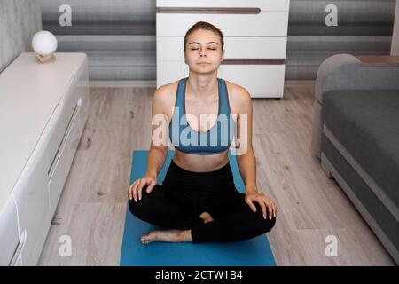 Yoga a casa. Mantenere la calma. Bella giovane donna seduta in posizione lotus con gli occhi chiusi. Foto Stock