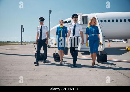 Due affascinanti stewardesses con capitano e secondo pilota fronte dell'aereo commerciale Foto Stock