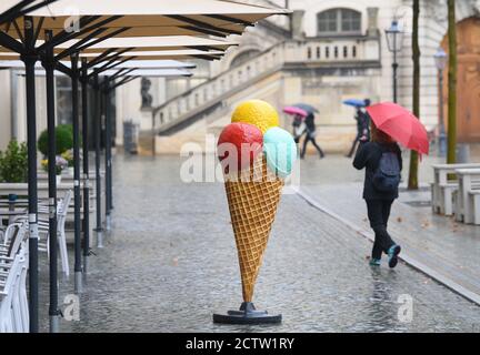 25 settembre 2020, Sassonia, Dresda: Una replica oversize di un cono gelato si erge sotto la pioggia sul Neumarkt mentre i passanti camminano con gli ombrelloni. Foto: Robert Michael/dpa-Zentralbild/ZB Foto Stock