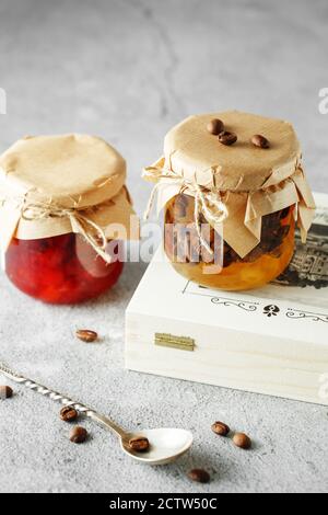 Due vasetti di marmellata di frutta fatta in casa. Marmellata di pere con chicchi di caffè e vasetto di marmellata di arancia su sfondo grigio chiaro. Foto Stock