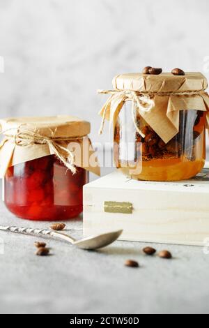 Due vasetti di marmellata di frutta fatta in casa. Marmellata di pere con chicchi di caffè e vasetto di marmellata di arancia su sfondo grigio chiaro. Foto Stock