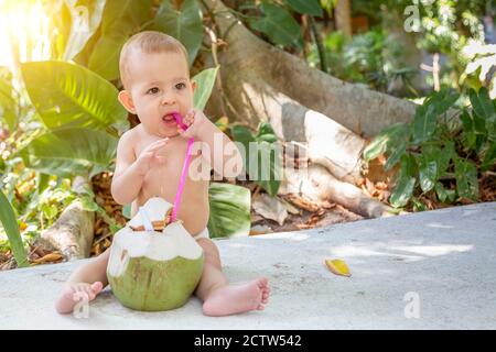 Bambino felice del bambino in vacanza tropicale. Mangia e beve di cocco verde giovane. Foto Stock