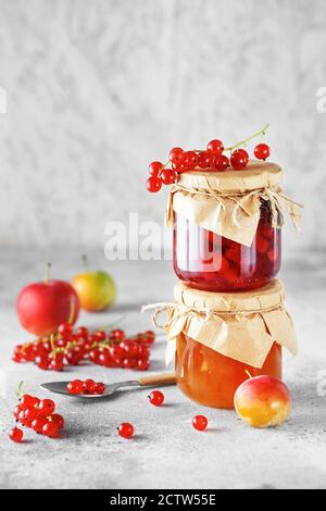 due vasetti di marmellata di frutta fatta in casa. Vasetti di vetro con diversi tipi di marmellata e bacche. Confettura di prugne e ribes rosso su sfondo grigio chiaro. Foto Stock