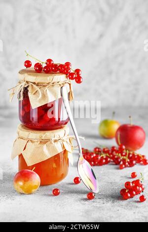 due vasetti di marmellata di frutta fatta in casa. Vasetti di vetro con diversi tipi di marmellata e bacche. Confettura di prugne e ribes rosso su sfondo grigio chiaro. Foto Stock