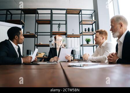 Una donna d'affari motivata tiene una riunione con i dipendenti alla scrivania dell'ufficio, scattando dal basso. Foto Stock