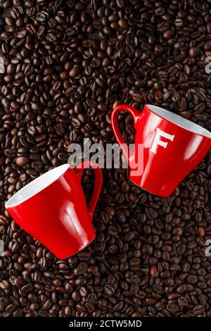 Chicchi di caffè nero in studio. Due tazze di caffè rosse sullo sfondo di chicchi di caffè appena tostati Foto Stock