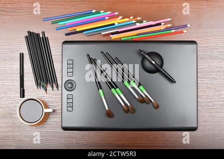 Tavoletta grafica professionale dall'alto con pennelli, penne digitali e multicolore. Isolato su sfondo di legno. Foto ad alta risoluzione. D. Piena Foto Stock