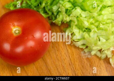 Foglie di lattuga a fette e un intero pomodoro maturo su una tavola di legno primo piano, vista dall'alto, spazio di copia Foto Stock