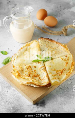 Pancake russi serviti con foglie di menta e ingredienti - latte e uova davanti a sfondo grigio. Fotografia alimentare Foto Stock