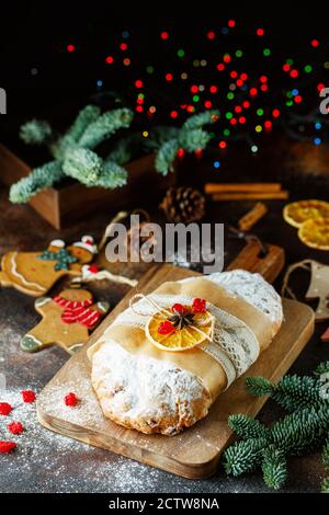 Cottura di festa. Torta di Natale. Composizione di stollen, rami di abete rosso, decorazioni per alberi di Natale, coni, fette secche di arance, bacche e spezie Foto Stock