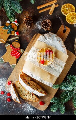 Cottura di festa. Torta di Natale. Composizione piatta di stollen, rami di abete rosso, decorazioni per alberi di Natale, coni, fette secche di arance, bacche e. Foto Stock