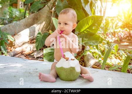 Bambino felice del bambino in vacanza tropicale. Bevande verde cocco giovane. Siede su un pavimento nella foresta pluviale. Foto Stock